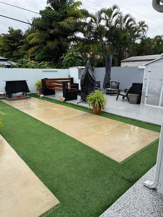 Outdoor space featuring a stamped concrete patio, synthetic lawn, solid-surface textured flooring, and perimeter privacy fencing