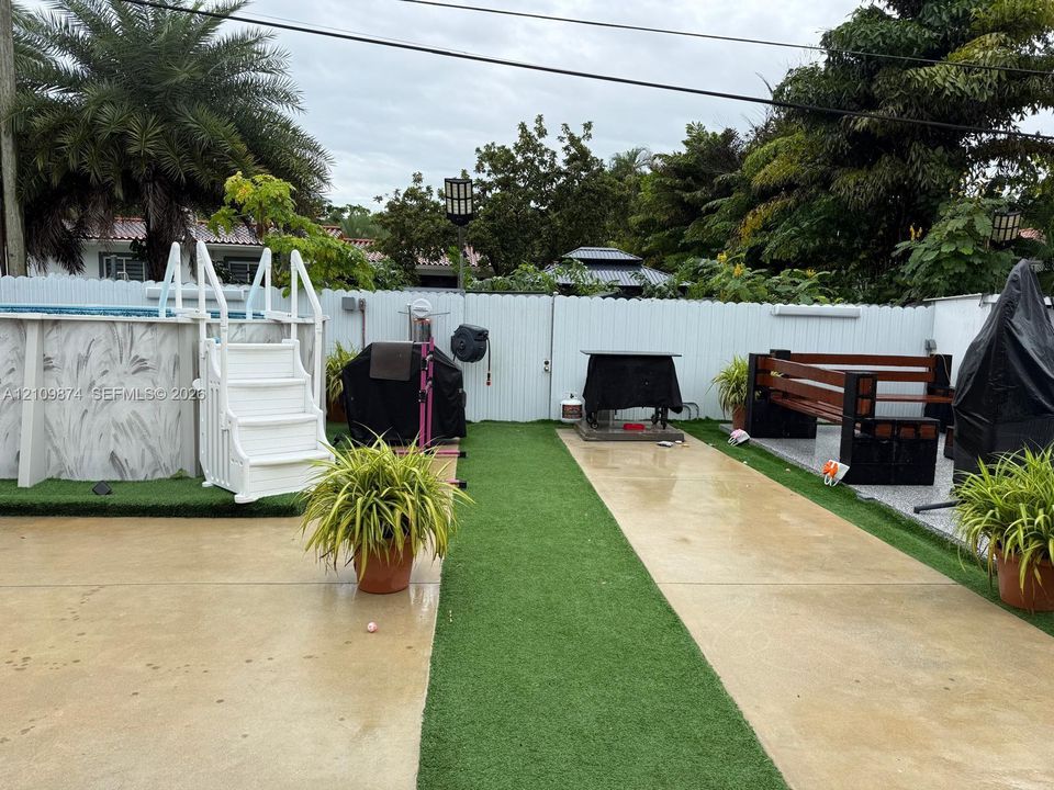 Backyard featuring a swimming pool with integrated staircase, artificial turf lawn, poured concrete walkways, and perimeter white vinyl fencing