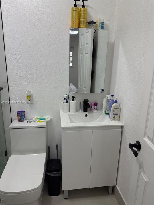 Compact vanity featuring a white cabinet base, integrated sink, and matte black faucet, paired with a wall-mounted mirrored medicine cabinet and a one-piece dual-flush toilet