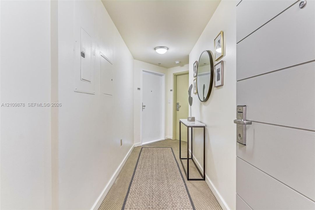 Entryway featuring a multi-panel door with a metallic lever handle, wall-mounted light fixture, and textured carpeting