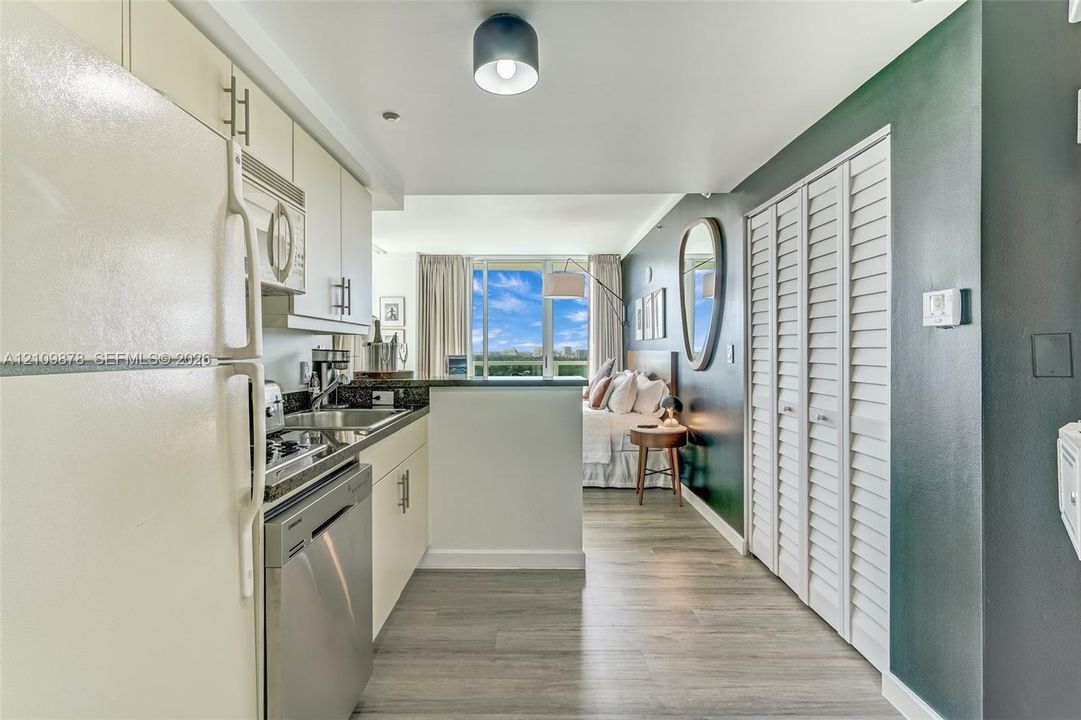 Kitchen area featuring wood-finish flooring, white cabinetry with silver-tone hardware, stainless steel dishwasher, and louvered closet doors