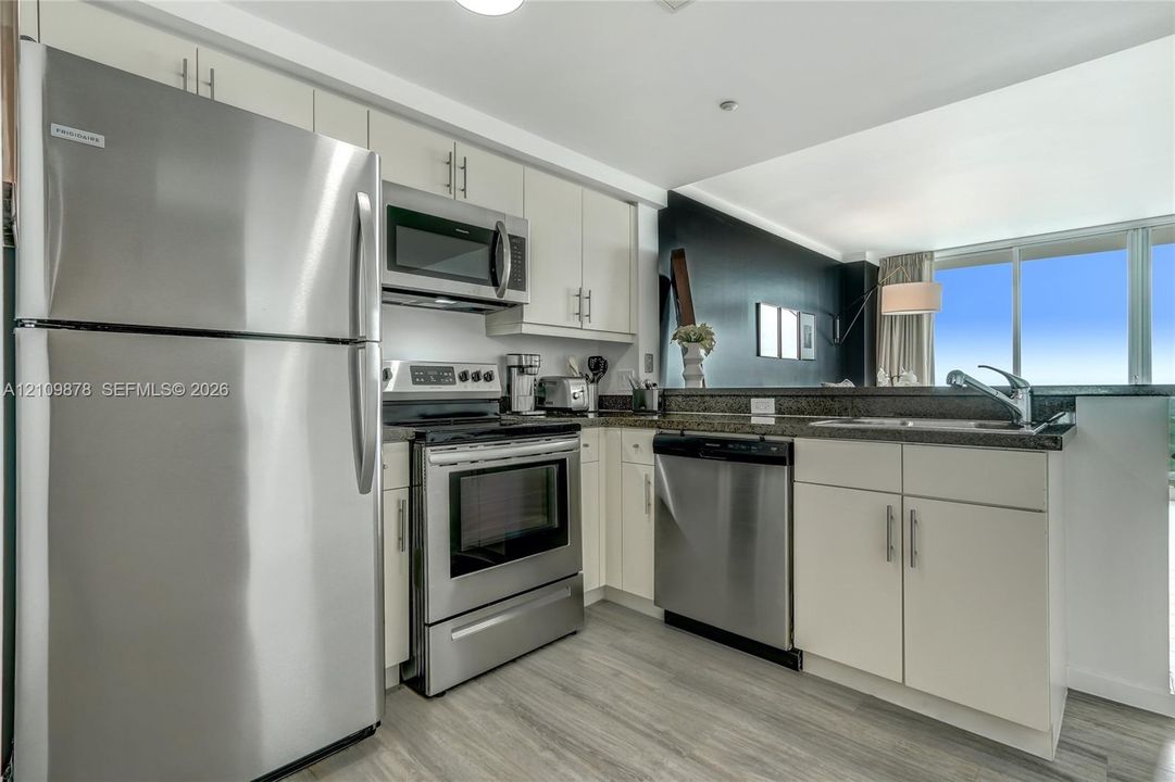 Kitchen featuring stainless steel appliances, neutral cabinetry with linear hardware, dark stone-finish countertops, and wood-finish flooring