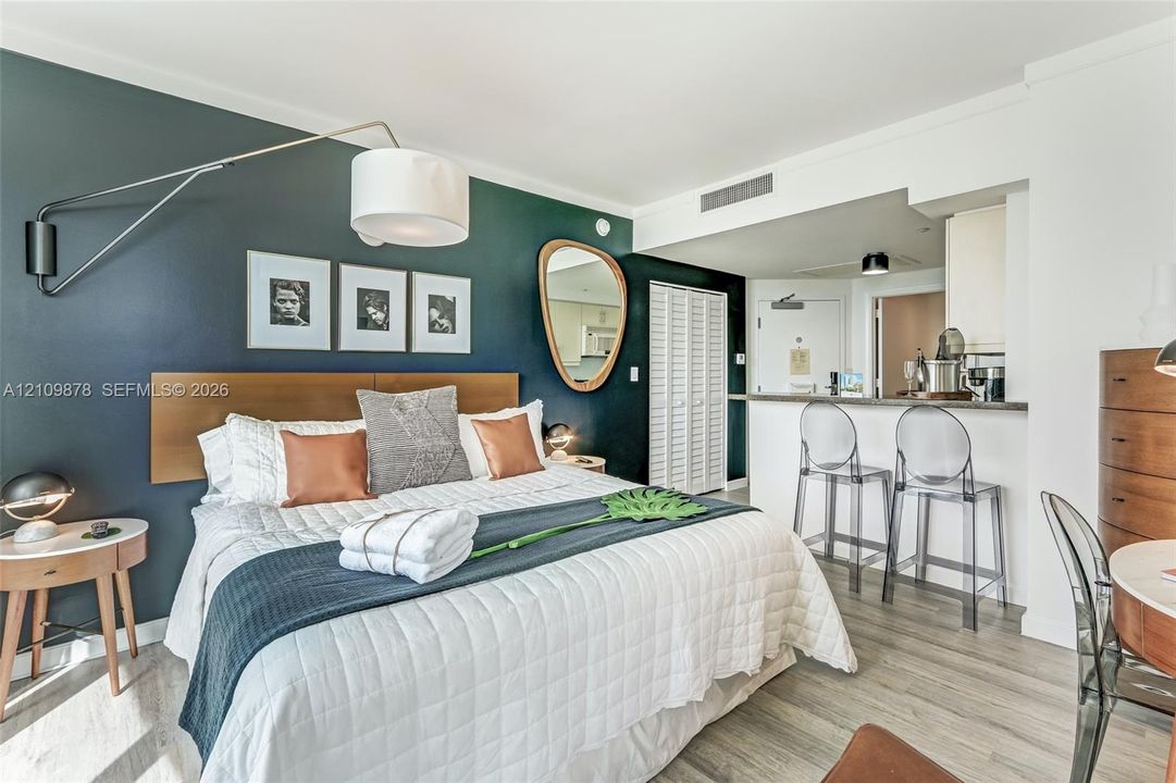 Dark-toned accent wall, wood-finish flooring, built-in breakfast bar with stone countertop, swinging wall-mounted light fixture, and floor-to-ceiling white louvered closet doors