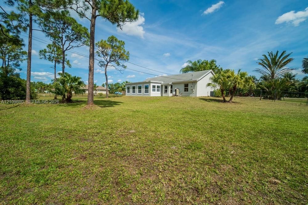 Expansive backyard featuring a sprawling lawn, mature pine trees, palm landscaping, and an exterior with an enclosed porch area