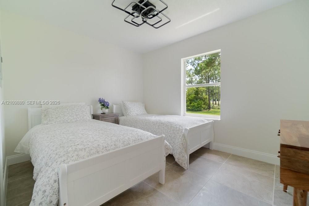 Neutral-toned room featuring large-format tile flooring, a geometric flush-mount ceiling light fixture, and a single-hung window with exterior tree-line scenery