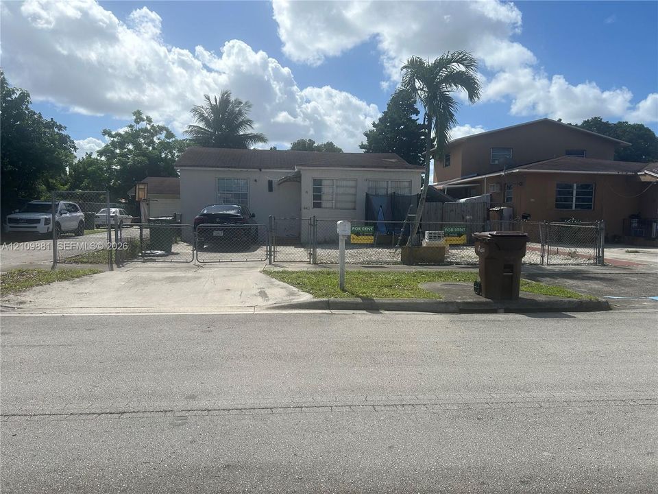 Single-story residence featuring a concrete driveway, metal chain-link fencing, and mature palm tree
