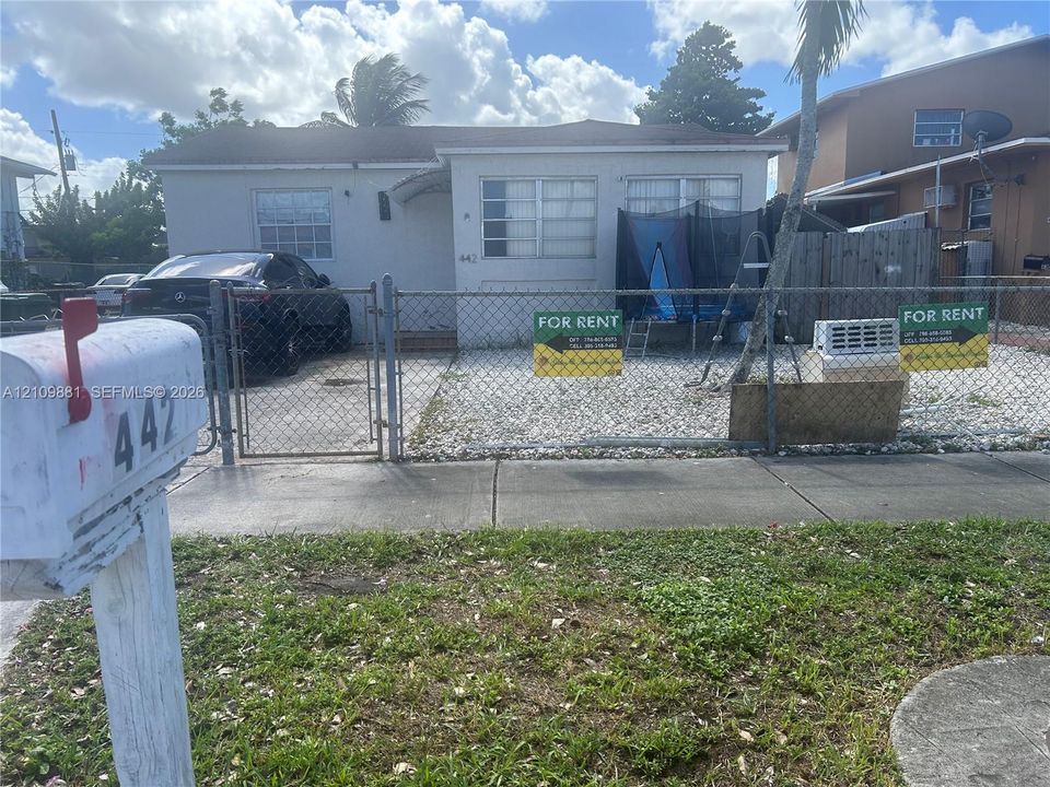 Single-story exterior featuring light-toned stucco siding, grid-pattern windows, and a chain-link fenced perimeter