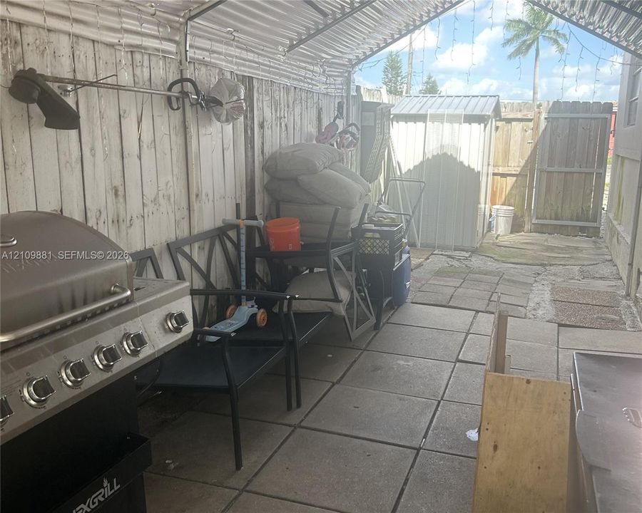 Covered patio area featuring concrete paver flooring, corrugated metal roofing, and wood fencing