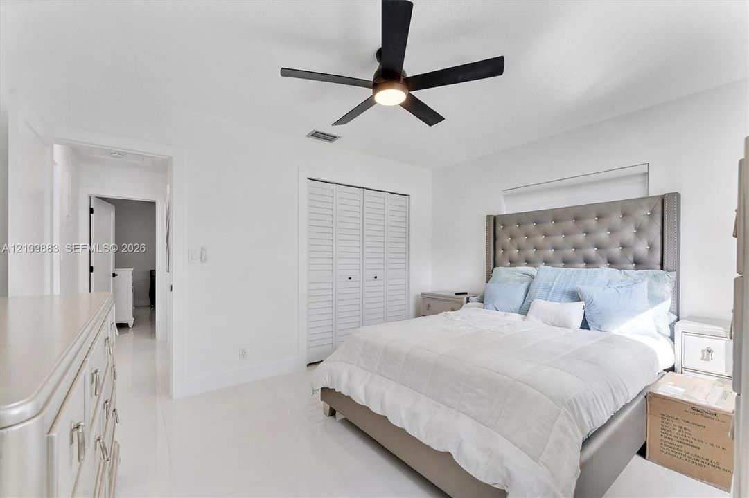 Bedroom featuring white tile flooring, white louvered closet doors, and a five-blade ceiling fan with integrated lighting