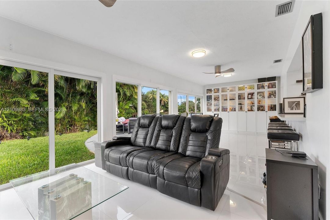 Open-concept living space featuring high-gloss tile flooring, floor-to-ceiling sliding glass doors, built-in white cabinetry, and recessed ceiling lighting