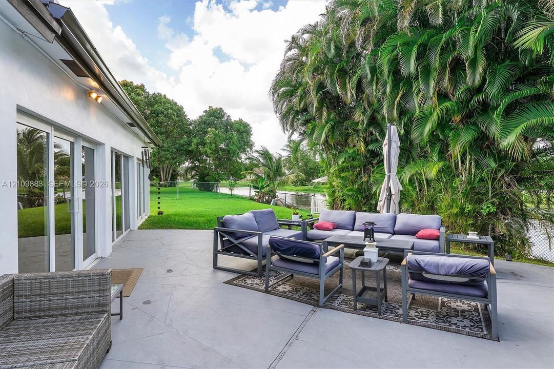 Concrete patio featuring sliding glass doors and expansive backyard greenery