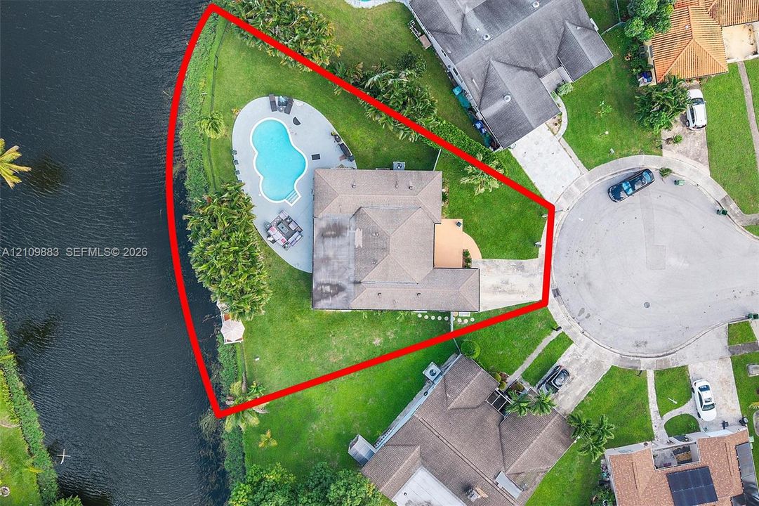 Waterfront lot on a cul-de-sac featuring a paved driveway, expansive lawn, and an in-ground swimming pool with surrounding deck
