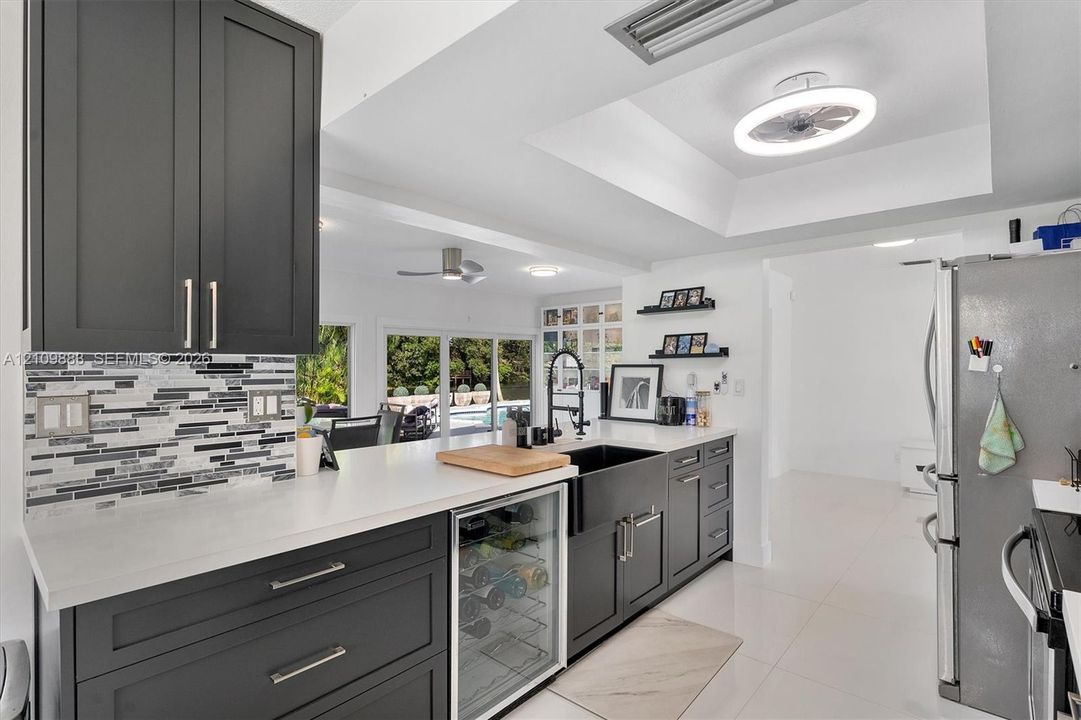 Kitchen featuring charcoal-toned shaker cabinetry, quartz countertops, a stone mosaic backsplash, integrated wine refrigerator, and a farmhouse-style sink with a high-arch faucet