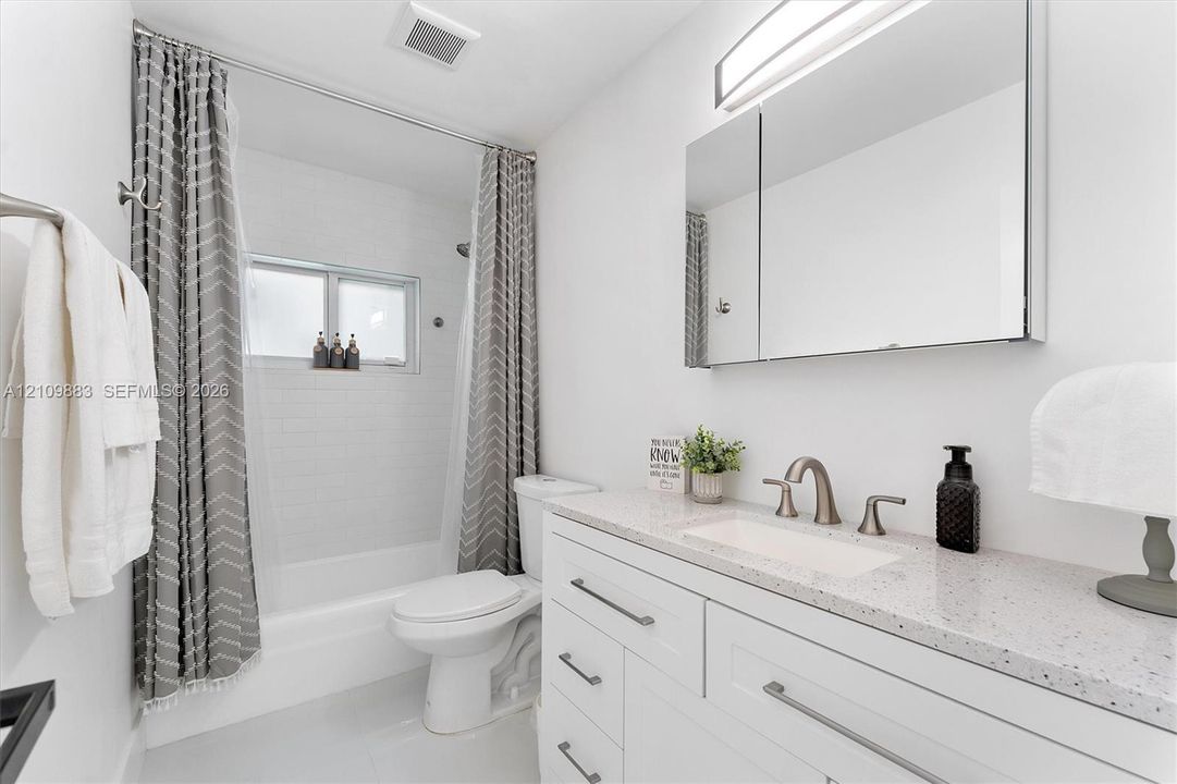 Bathroom featuring a vanity with a light-toned speckled countertop, an undermount sink, brushed nickel faucet hardware, a mirrored medicine cabinet, and a tiled tub-shower surround
