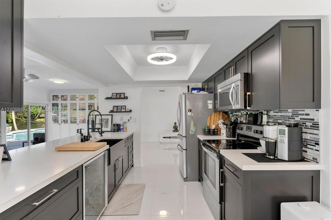 Kitchen featuring charcoal-toned cabinetry, quartz countertops, a farmhouse-style sink with a high-arch faucet, a built-in beverage refrigerator, and a linear mosaic tile backsplash