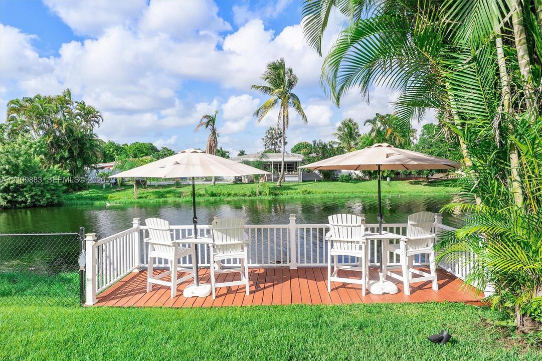 Waterfront deck featuring wood-finish flooring, white picket railing, and manicured landscaping