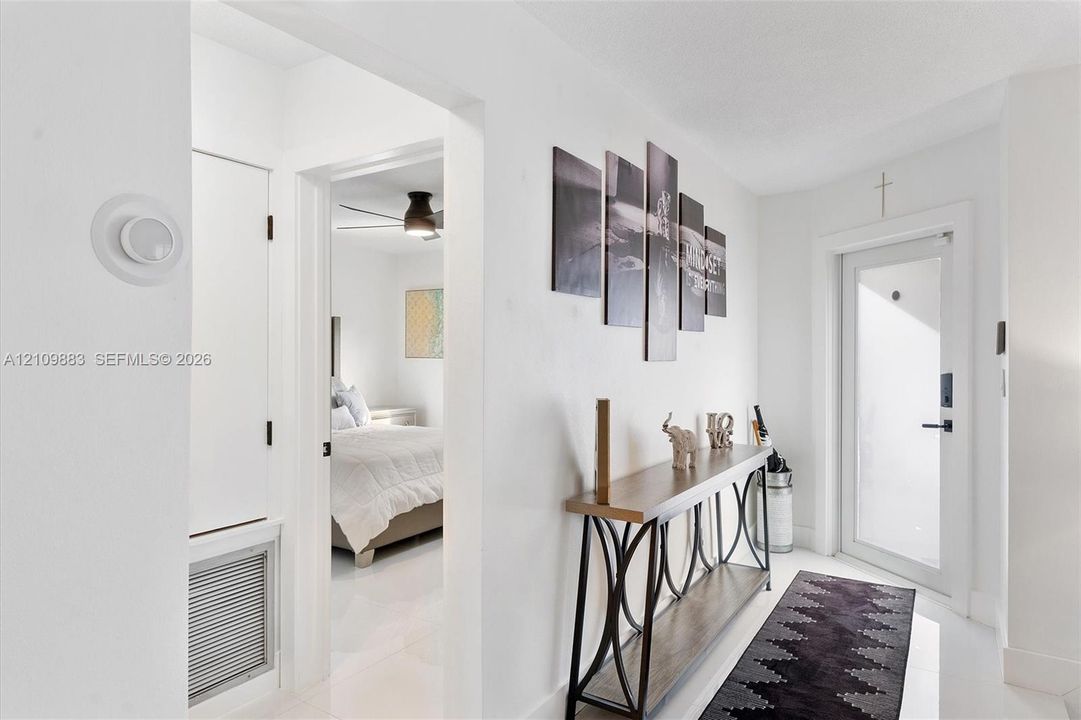 Entryway featuring crisp white walls, neutral tile flooring, a glass-panel entry door, and a built-in ventilation intake