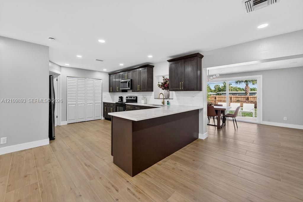 Kitchen featuring dark wood cabinetry, quartz countertops, a breakfast bar, recessed lighting, and wood-finish flooring