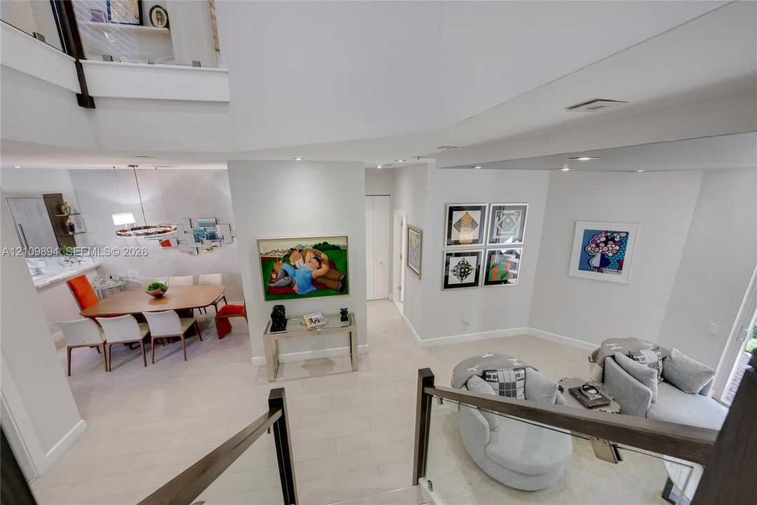 Open-concept living space featuring high ceilings, neutral-toned flooring, glass panel stair railing, and recessed lighting