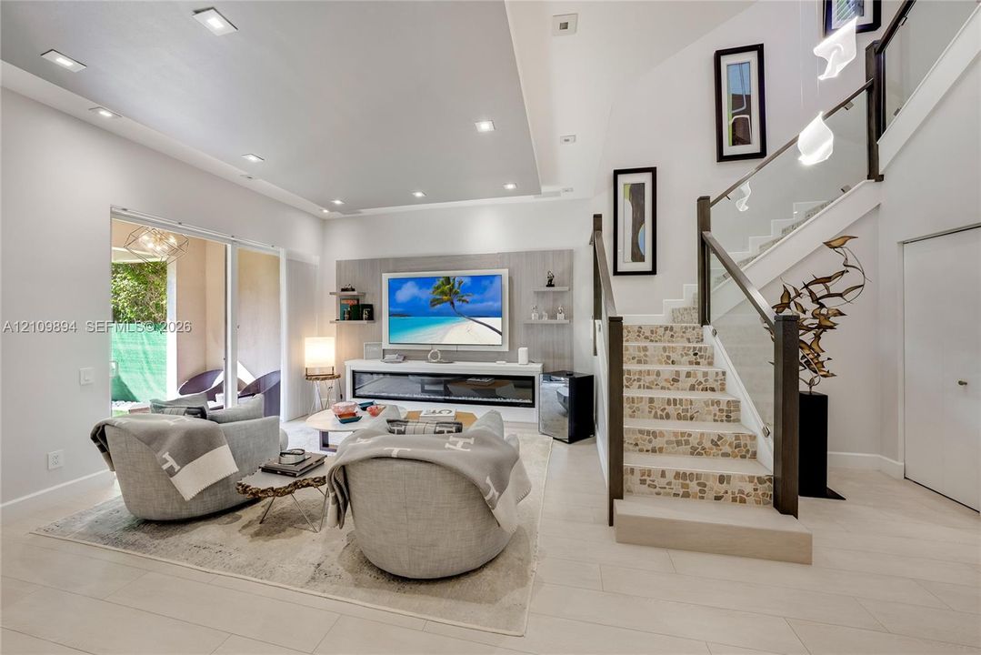 Living area featuring recessed lighting, a built-in linear fireplace with surround shelving, tile-finish flooring, and a staircase with glass railings and decorative stone-tile treads