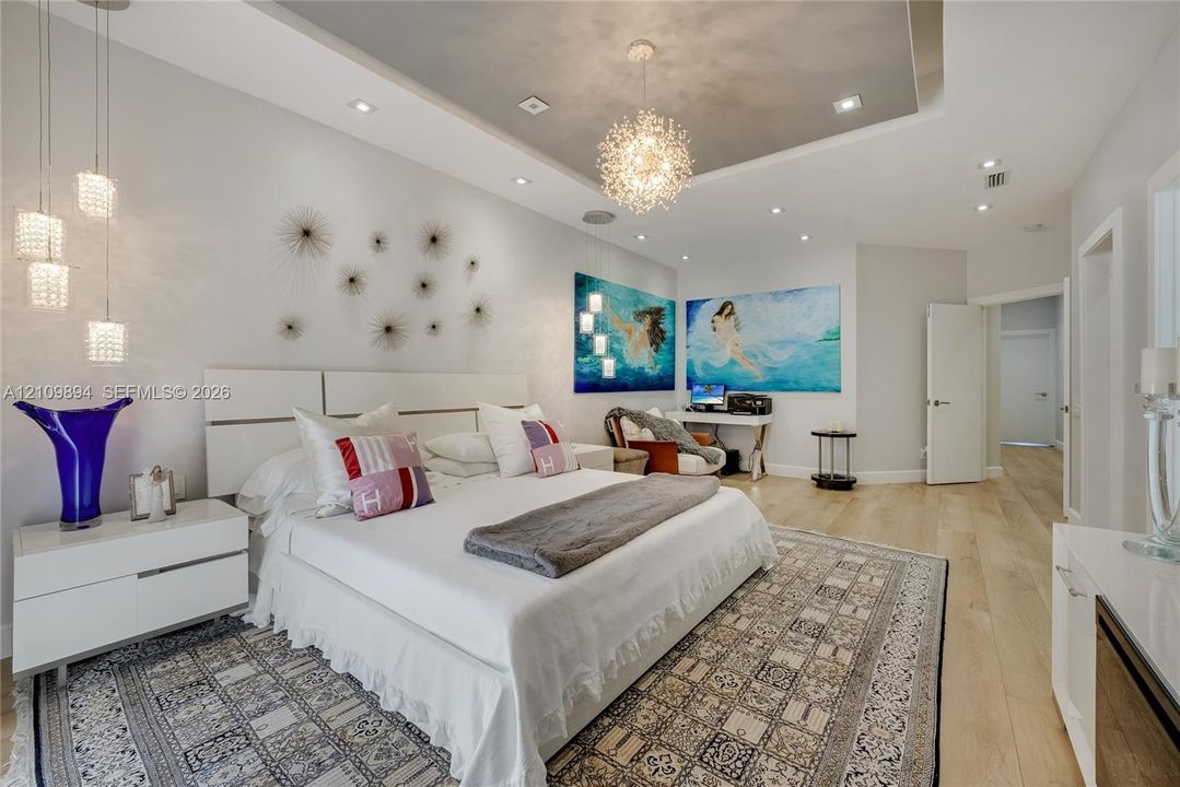 Tray ceiling featuring recessed lighting and a central decorative pendant, accompanied by wood-finish flooring and modern multi-light wall fixtures
