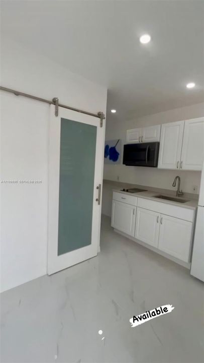 Sliding door with frosted glass panel, recessed ceiling lighting, white cabinetry, integrated microwave, and stone-finish flooring