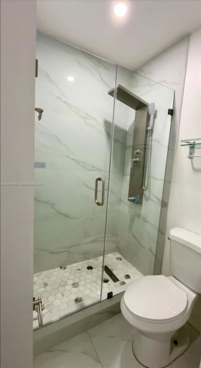Walk-in shower featuring large-format stone-pattern wall tile, frameless glass enclosure, recessed linear shower system, and hexagonal mosaic floor tiling