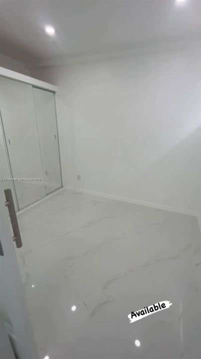 High-gloss stone-finish tile flooring, recessed ceiling lighting, and built-in sliding-door closet featuring mirrored panels