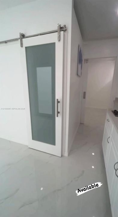 Sliding barn door featuring a white frame, frosted glass panel, and polished metallic hardware, set against large-format, white stone-finish flooring with grey veining
