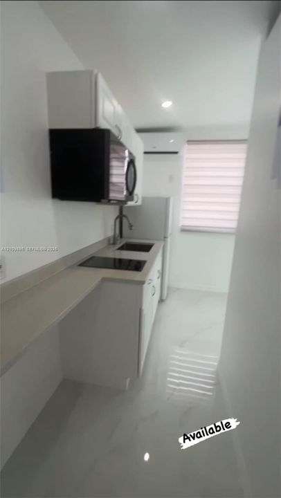 Kitchen featuring white cabinetry, solid-surface countertops, a recessed sink with a gooseneck faucet, a built-in cooktop, and polished tile flooring
