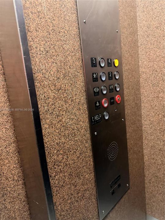 Elevator cabin featuring a brushed metal control panel with integrated push-button interface, emergency help communication system, and textured interior paneling