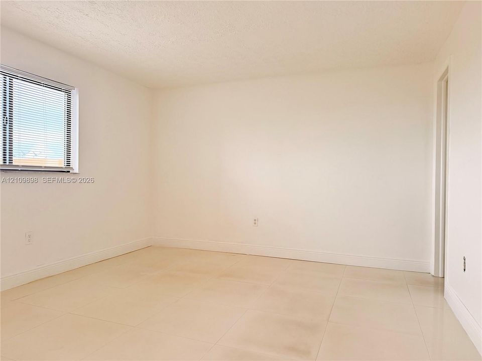 Neutral interior room featuring oversized floor tile and a window with horizontal blinds