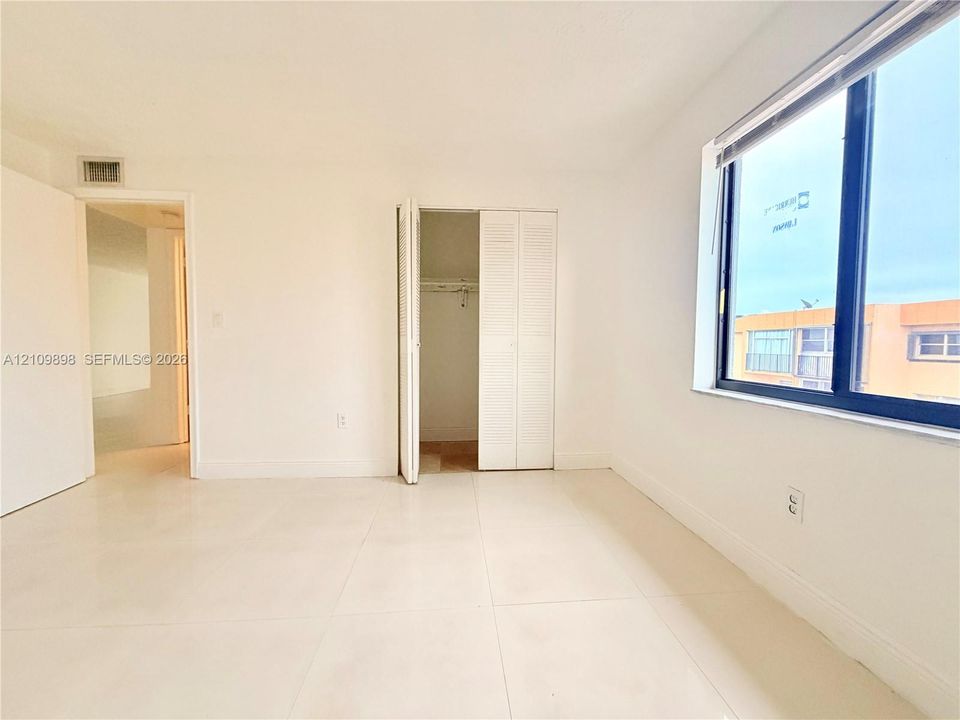 Interior space featuring large-format tile flooring, a window with a dark metal frame, and a built-in closet with louvered bifold doors