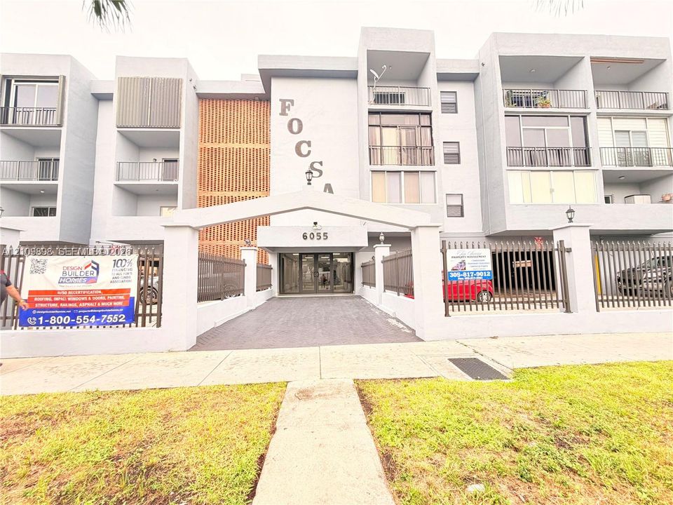 Multi-story facade featuring concrete construction, metal balcony railings, decorative wood-slat screening, and a gated entrance with a paved driveway