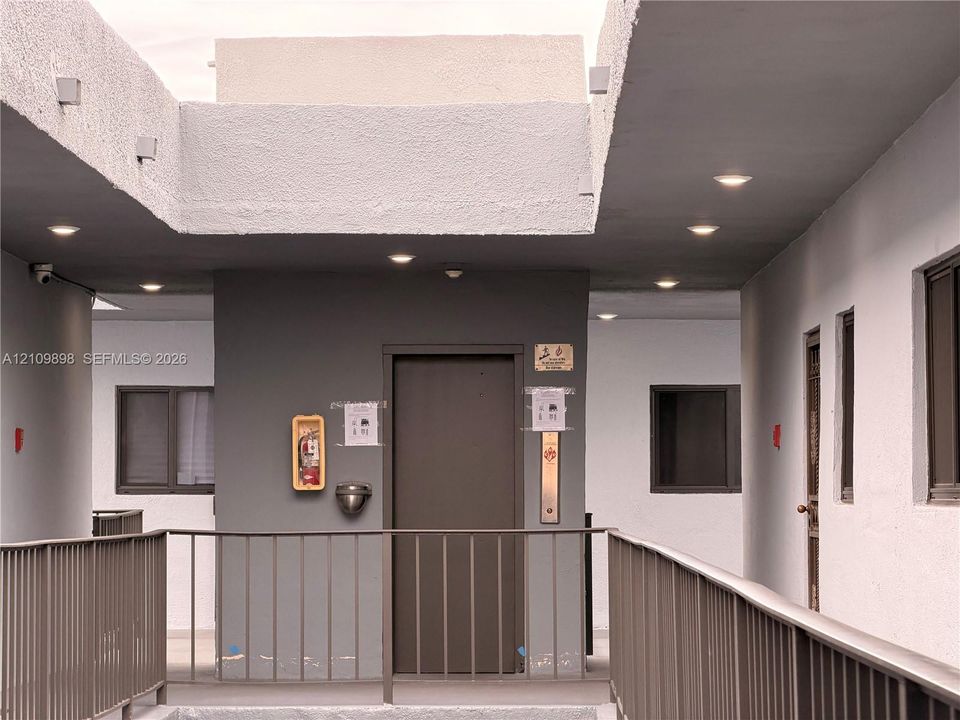 Covered exterior corridor featuring recessed ceiling lighting, metal safety railings, and neutral textured walls