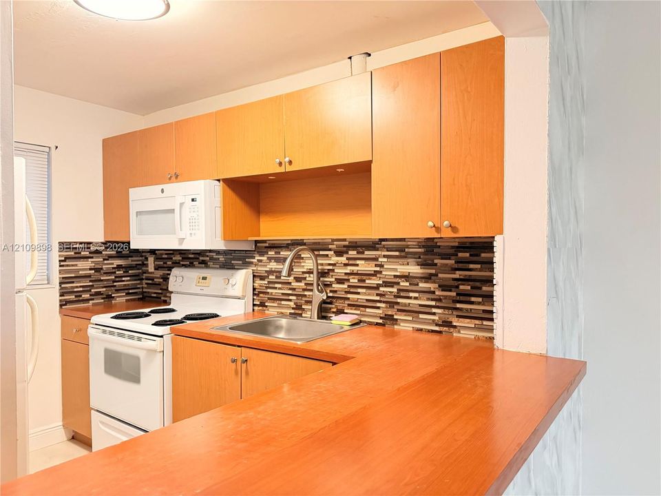 Kitchen featuring flat-panel wood-finish cabinetry, multi-tonal horizontal tile backsplash, stainless steel sink with high-arc faucet, and attached peninsula counter