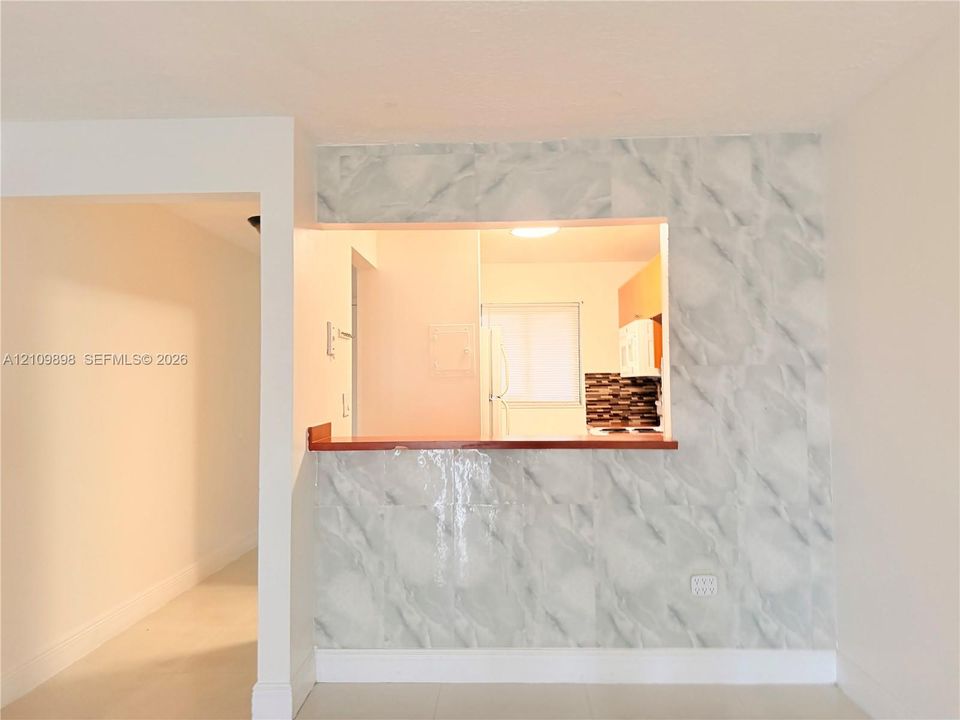 Pass-through opening featuring a natural-finish wood countertop, stone-patterned tile wall facade, and neutral-toned flooring