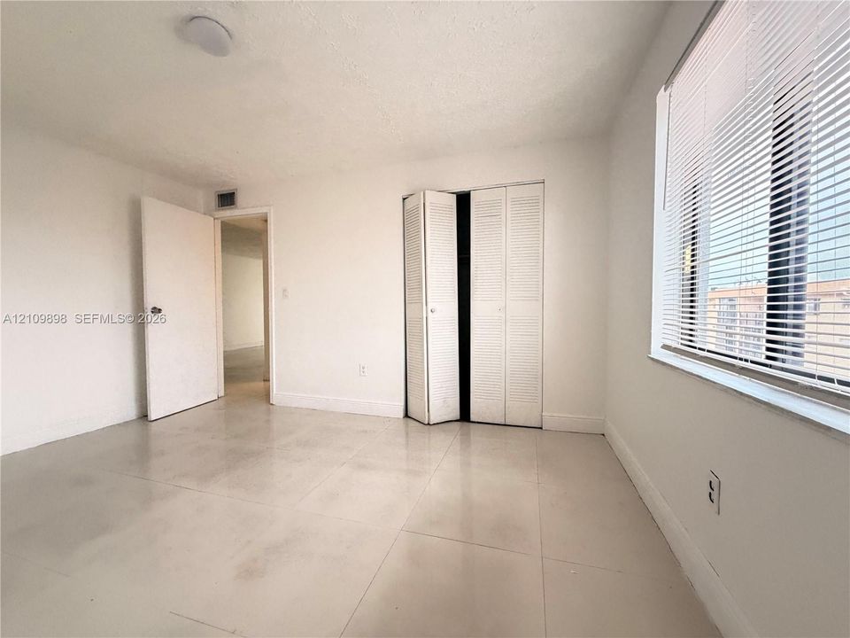 Neutral-toned tile flooring, bi-fold louvered closet doors, and large windows with horizontal blinds