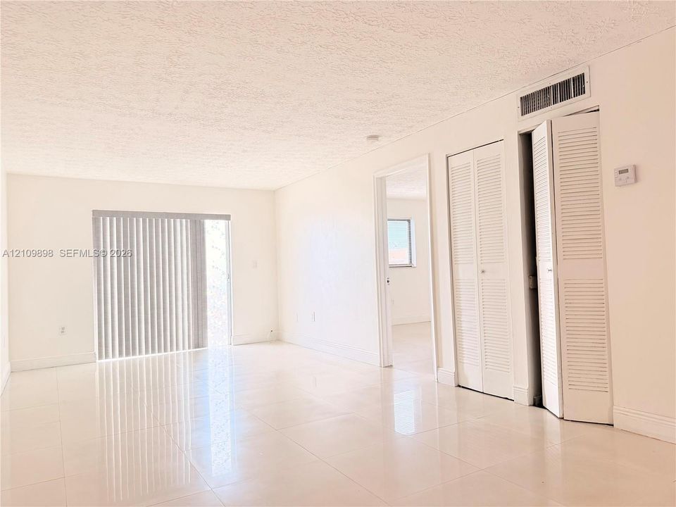 Neutral-toned tile flooring, floor-to-ceiling sliding glass doors with vertical blinds, and double-door closets with louvered panels