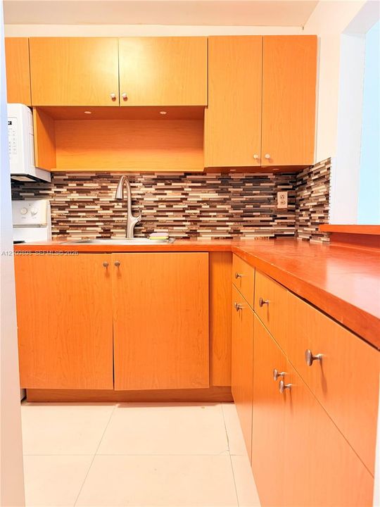 Kitchen featuring flat-panel wood cabinetry, tiered mosaic tile backsplash, countertop with integrated sink, pull-down faucet, and neutral floor tiling