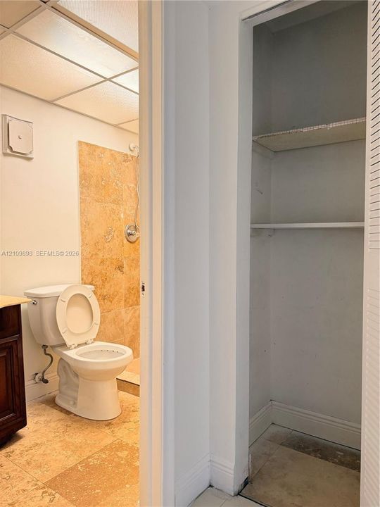 Bathroom featuring natural stone tile flooring, a stone-surround shower, wood-finish cabinetry, and a walk-in storage closet with built-in shelving