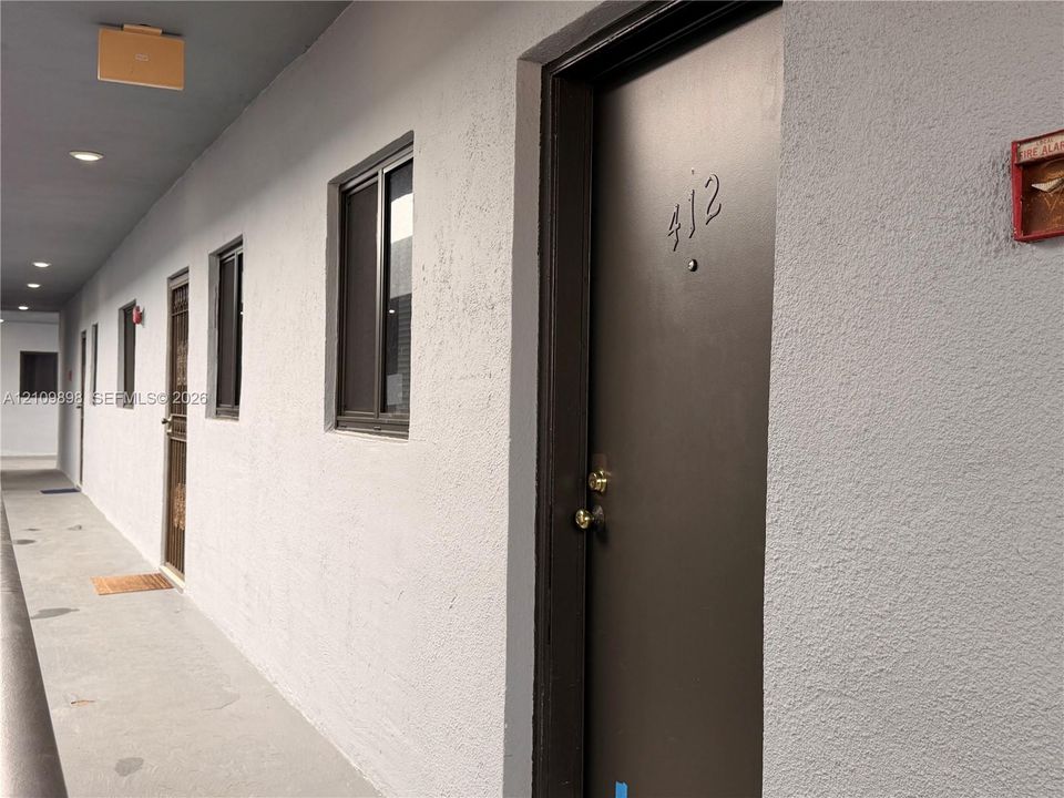 Exterior corridor with textured stucco walls, dark-toned entry doors, and recessed ceiling lighting