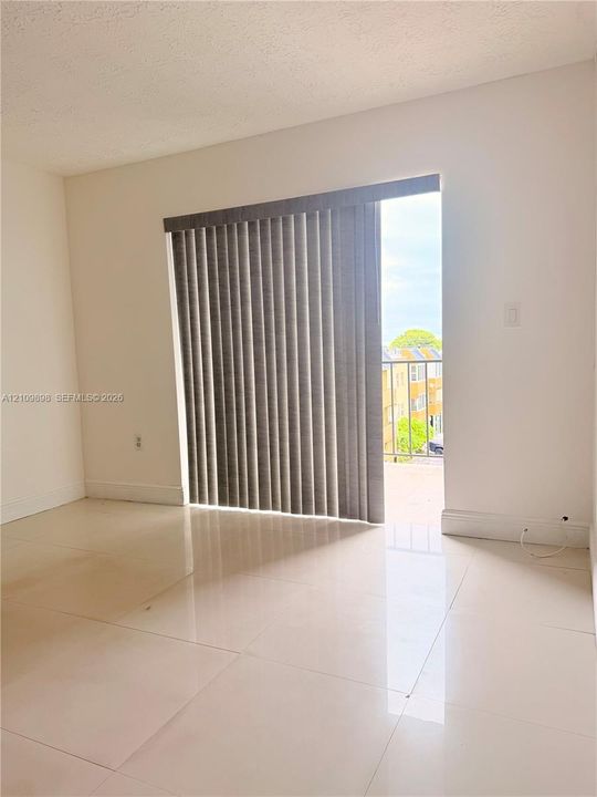 Large-format tile flooring, sliding glass door with vertical blinds, and metal balcony railing