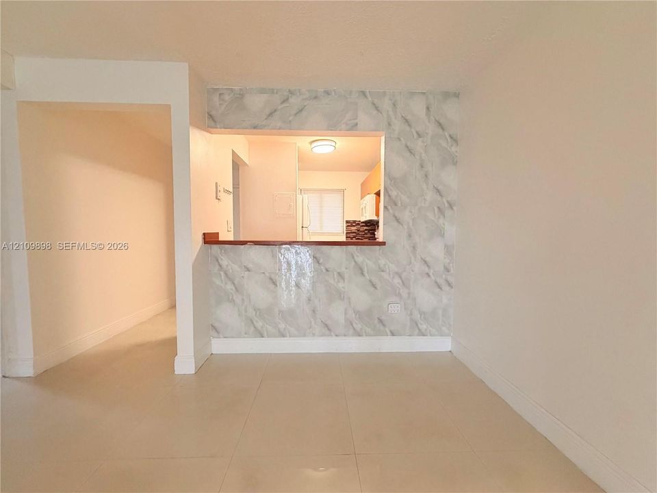 Pass-through kitchen counter with wood-finish ledge and stone-patterned tile wall cladding, featuring neutral large-format tile flooring and recessed ceiling lighting
