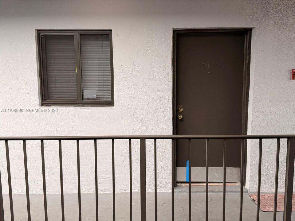Exterior entrance featuring a solid metal door with kick plate, horizontal sliding window with dark frames, and metal railing