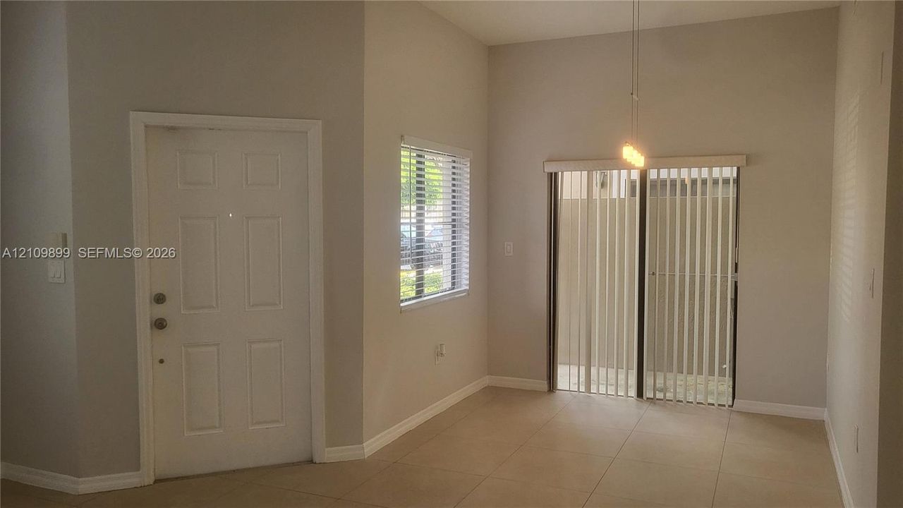 High ceilings featuring a hanging pendant light fixture, tile flooring, sliding glass doors, and a window with horizontal blinds