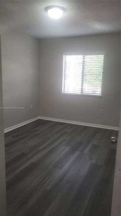 Room featuring wood-finish flooring, neutral wall paint, and window with integrated blinds