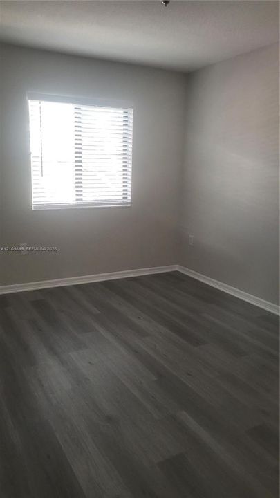 Room featuring wood-finish flooring, neutral wall paint, and a window equipped with horizontal blinds