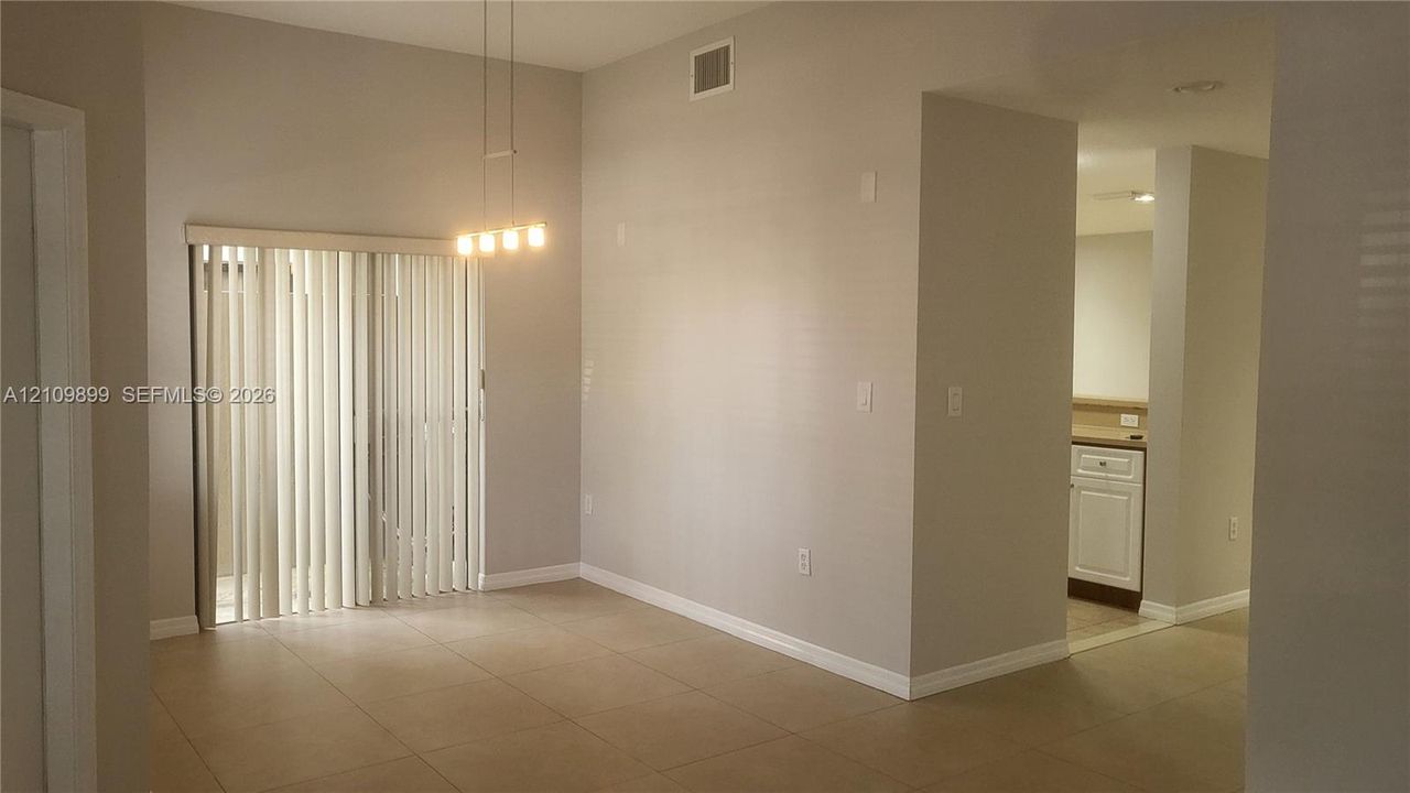 High-ceiling interior featuring tile flooring, sliding glass doors, a multi-light pendant fixture, and white cabinetry