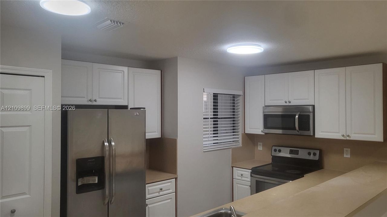 Kitchen featuring white shaker-style cabinetry, stainless steel appliances, neutral countertops, and flush-mount ceiling lighting
